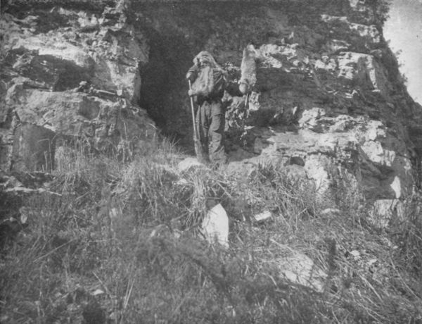 AN AGED PROSPECTOR AT MOUTH OF HIS MINE